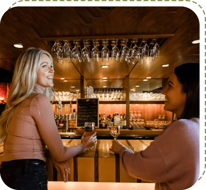 Two women are standing at a bar talking.